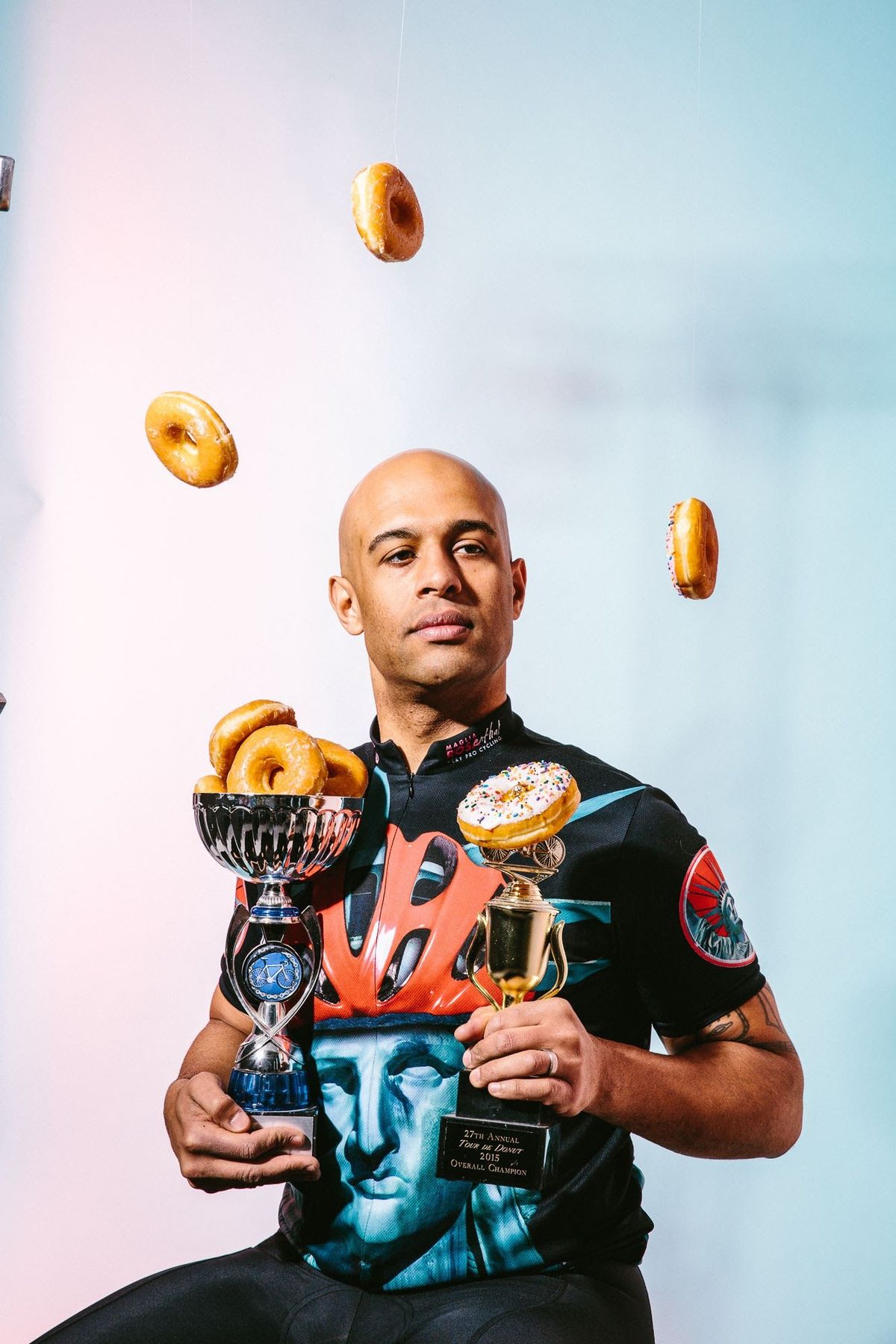 Yasir Salem in a cycling jersey holding two donut-filled trophies while donuts fly through the air
